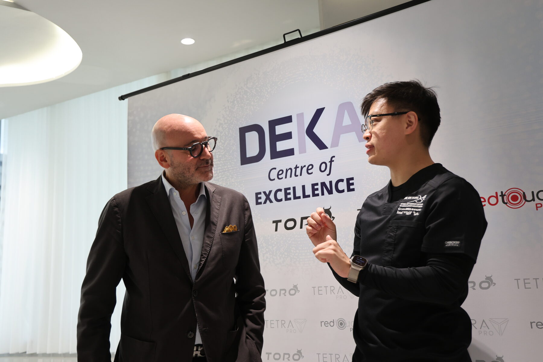 Dr Sin Yong in conversation with a DEKA representative at the DEKA Centre of Excellence backdrop, Singapore